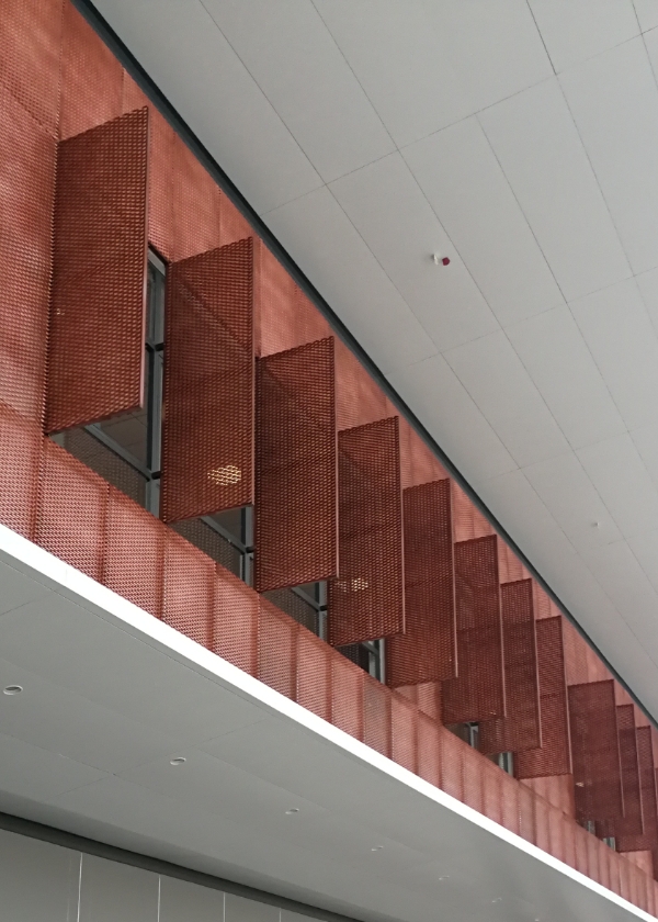 红色的装饰钢板网安装在建筑的窗户部位，下面有行人走过。