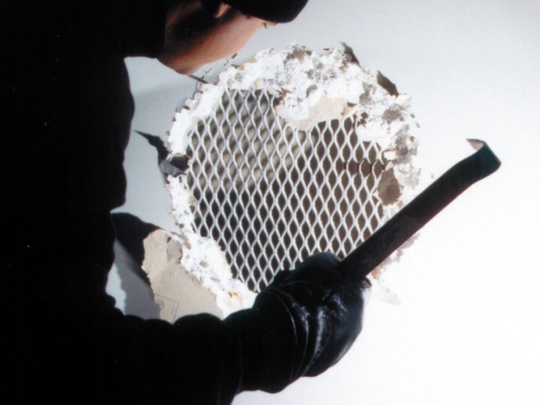 一个穿黑色衣服的人手拿工具将石膏墙凿开，中间漏出钢板网。